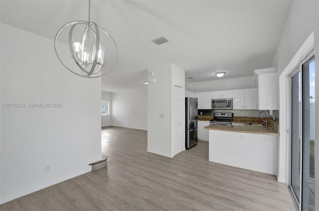 Kitchen featuring white cabinetry, stone countertops, stainless steel appliances, wood-finish flooring, and a circular geometric chandelier
