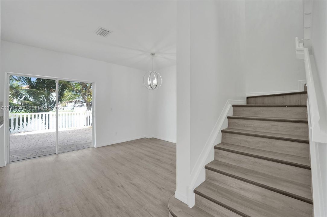 Wood-finish flooring throughout, staircase with wood-finish treads, spherical pendant light fixture, and sliding glass door leading to a paved patio