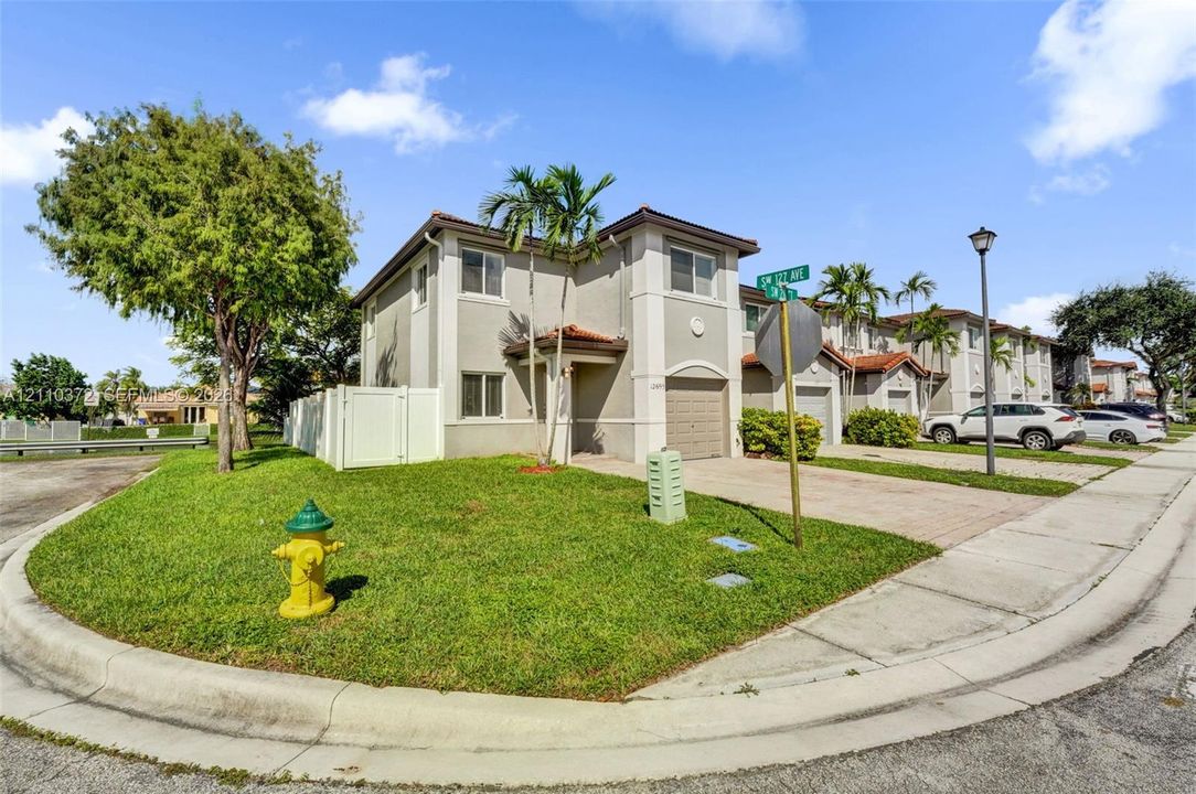 Two-story stucco exterior featuring a tiled roof, paver driveway, single-car garage, and corner lot positioning