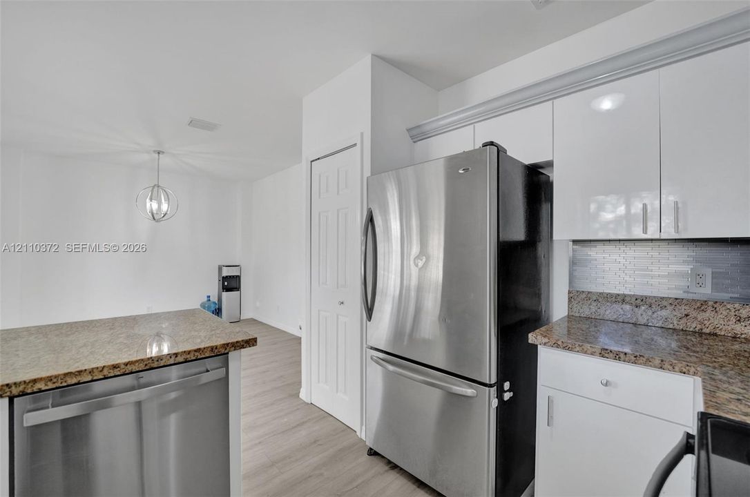 Kitchen featuring high-gloss white cabinetry, stone countertops, stainless steel appliances, and wood-finish flooring