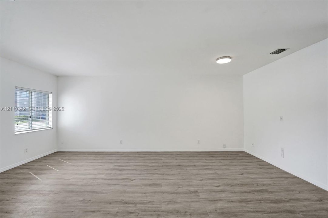 Interior space featuring wood-finish flooring, white walls, and a single-pane window with horizontal blinds