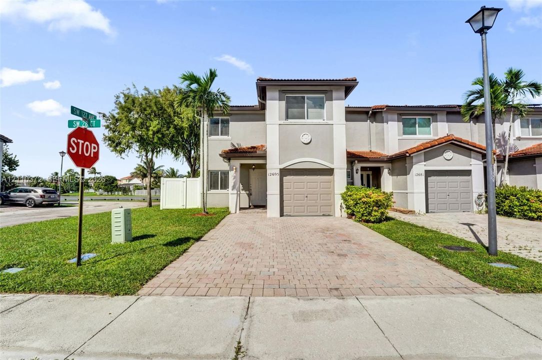 Multi-level exterior featuring a stucco facade, tile roofing, paver driveway, attached garage, and landscaping
