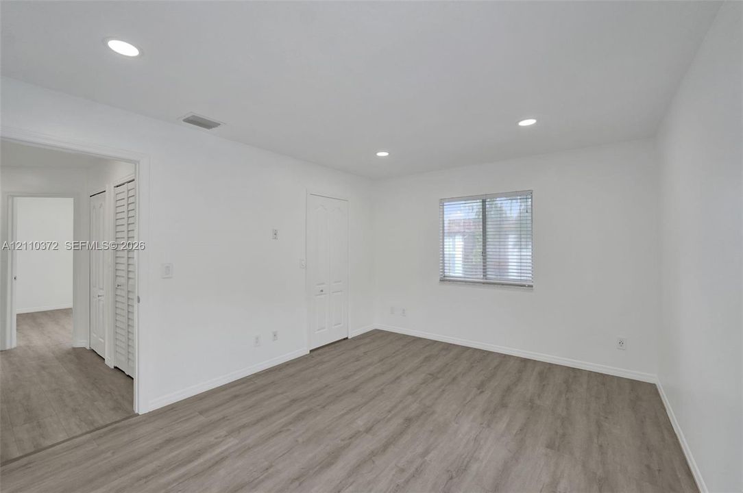 Room featuring wood-finish flooring, recessed lighting, and white interior doors with louvered closet panels