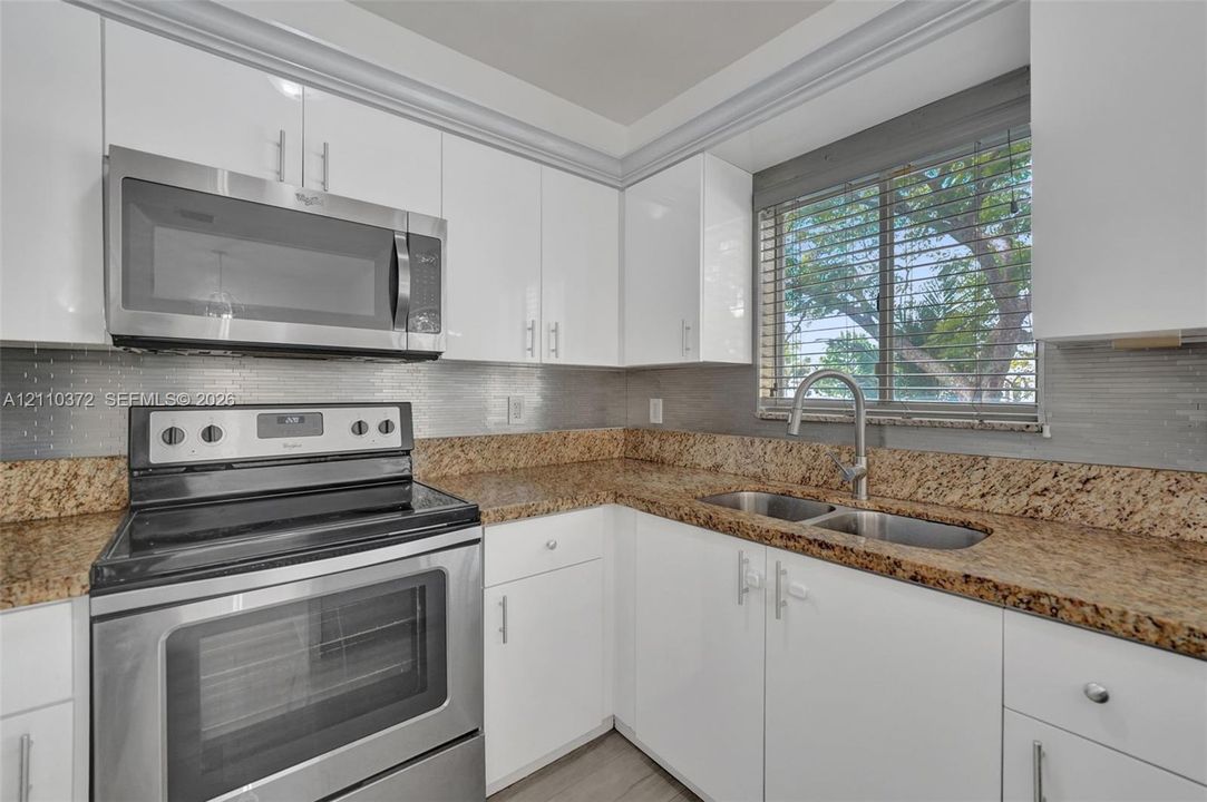 Kitchen featuring white cabinetry, stone countertops, stainless steel appliances, a horizontal tile backsplash, and a dual-basin undermount sink with a gooseneck faucet