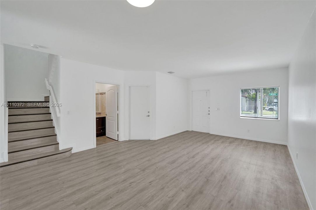 Open-concept interior featuring neutral wall tones, wood-finish flooring, a staircase with white railings, and a single-pane window