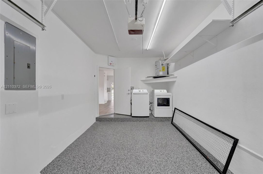 Garage space featuring epoxy-coated flooring, built-in shelving, linear LED lighting, and an integrated laundry hookup area