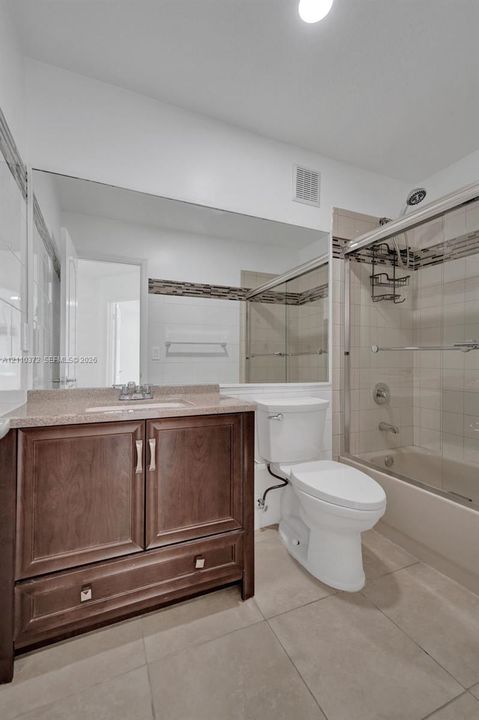 Bathroom featuring a wood-tone vanity, solid-surface countertop, full-width wall mirror, tile flooring, and a glass-enclosed tub and shower combination