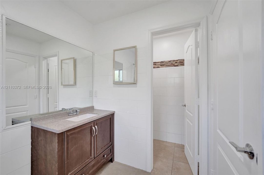 Bathroom vanity with dark wood-finish cabinetry, stone-composite countertop, rectangular undermount sink, and large wall-mounted mirror
