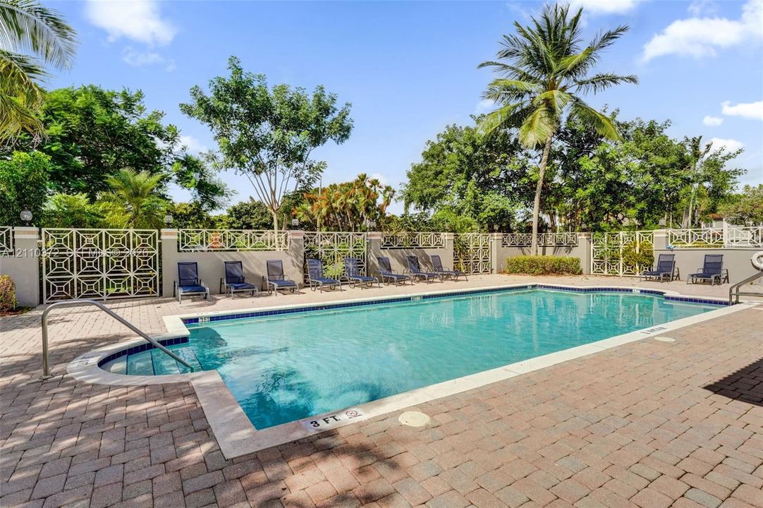 Swimming pool with a paved brick deck, built-in metal handrail, and decorative perimeter fencing, surrounded by mature palm trees and established landscaping