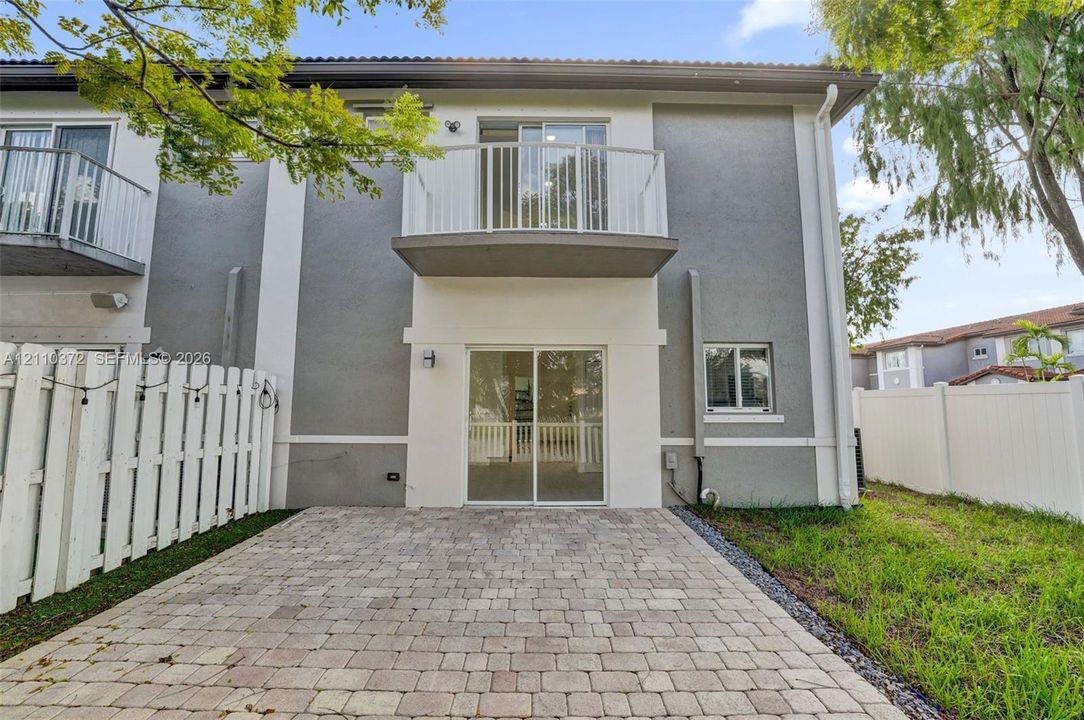 Exterior featuring a paver patio, second-story balcony with metal railing, sliding glass doors, and white vinyl privacy fencing