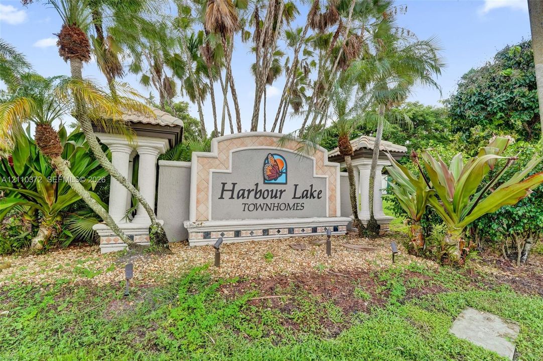 Community monument sign featuring decorative masonry pillars, stucco construction, and professional landscaping with palm trees