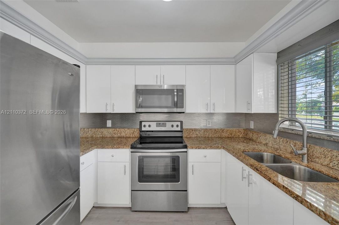 Kitchen featuring white cabinetry, stone-surface countertops, stainless steel appliances, a double-basin stainless steel sink, and crown molding