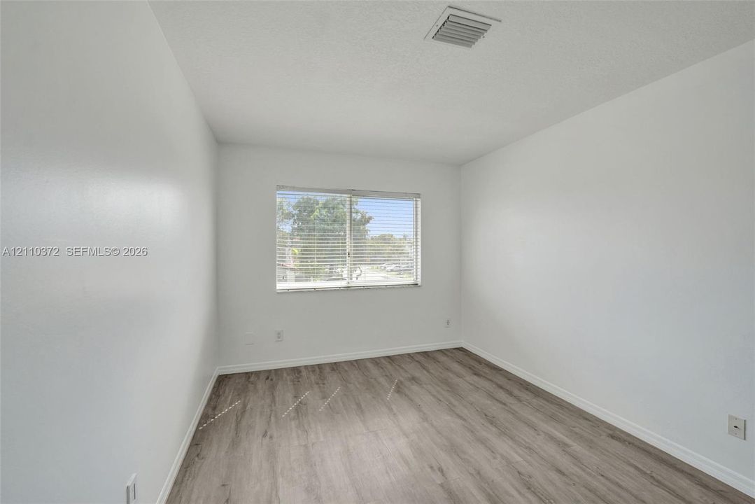 Room featuring wood-finish flooring, neutral walls, and a window with horizontal blinds