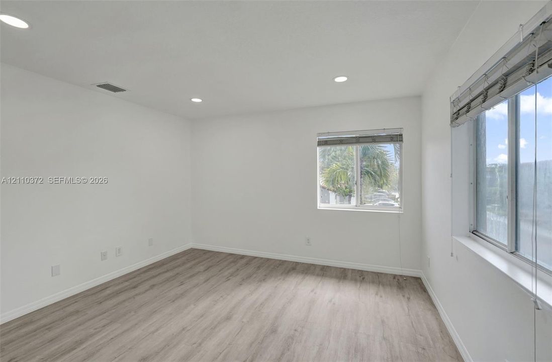 Neutral-toned interior room featuring wood-finish flooring, recessed lighting, and multiple windows