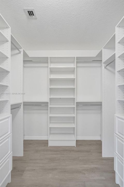 Walk-in closet featuring white built-in shelving, integrated dresser drawers, metal clothing rods, and wood-finish flooring
