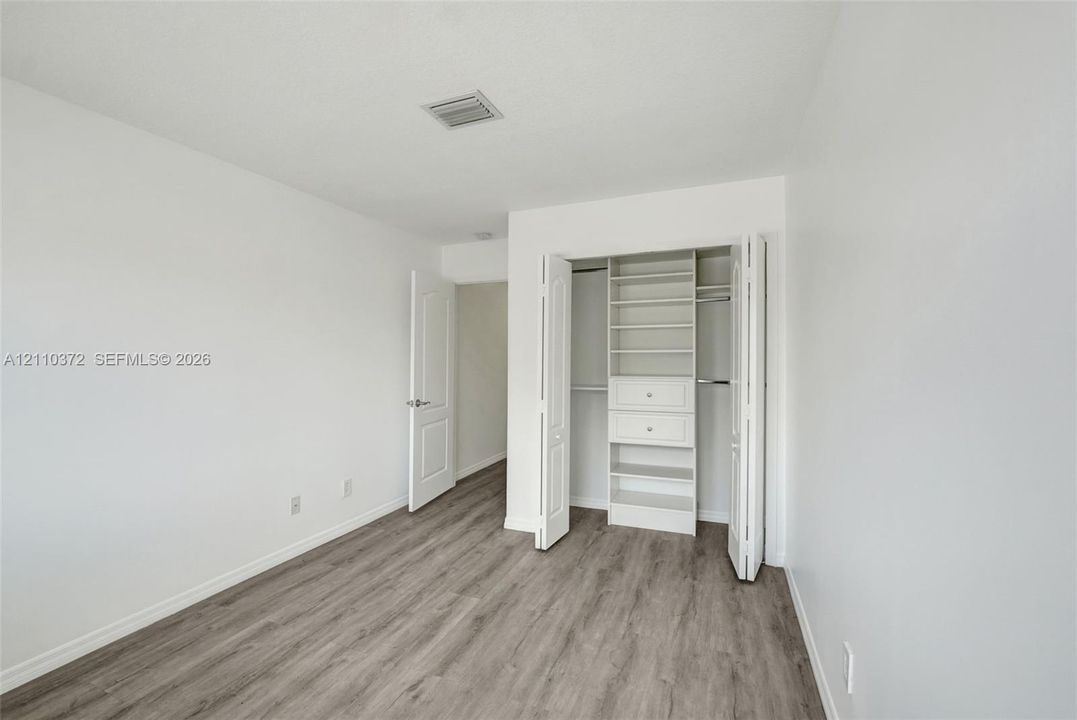 Room featuring wood-finish flooring, bi-fold closet doors, and a built-in closet organization system with shelving and drawers