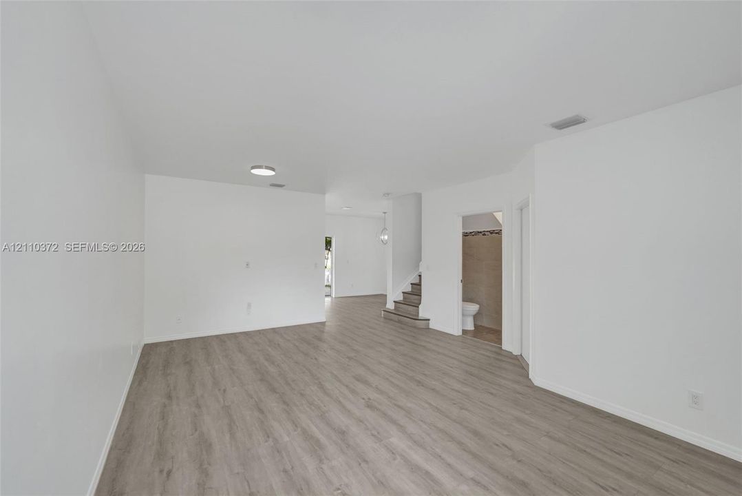 Open-concept interior featuring wood-finish flooring, neutral walls, recessed ceiling lighting, and a staircase