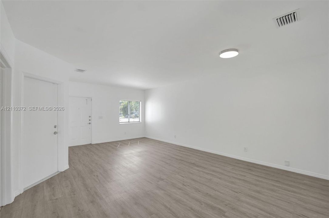 Open-concept interior featuring wood-finish flooring, a single-panel front door, and a flush-mount ceiling light