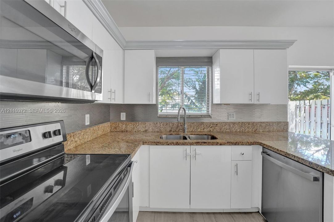 Kitchen featuring white flat-panel cabinetry, stone countertops, stainless steel appliances, a double-basin undermount sink, and horizontal tile backsplash