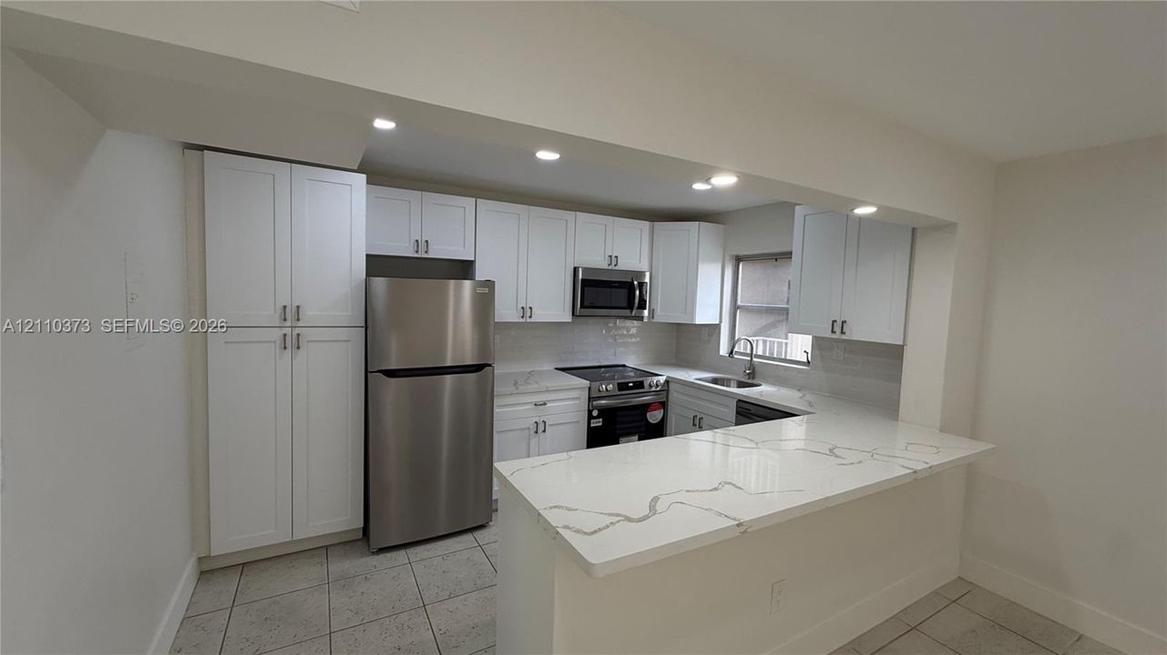 Kitchen featuring white cabinetry, quartz countertops with veining, stainless steel appliances, recessed ceiling lighting, and tiled flooring