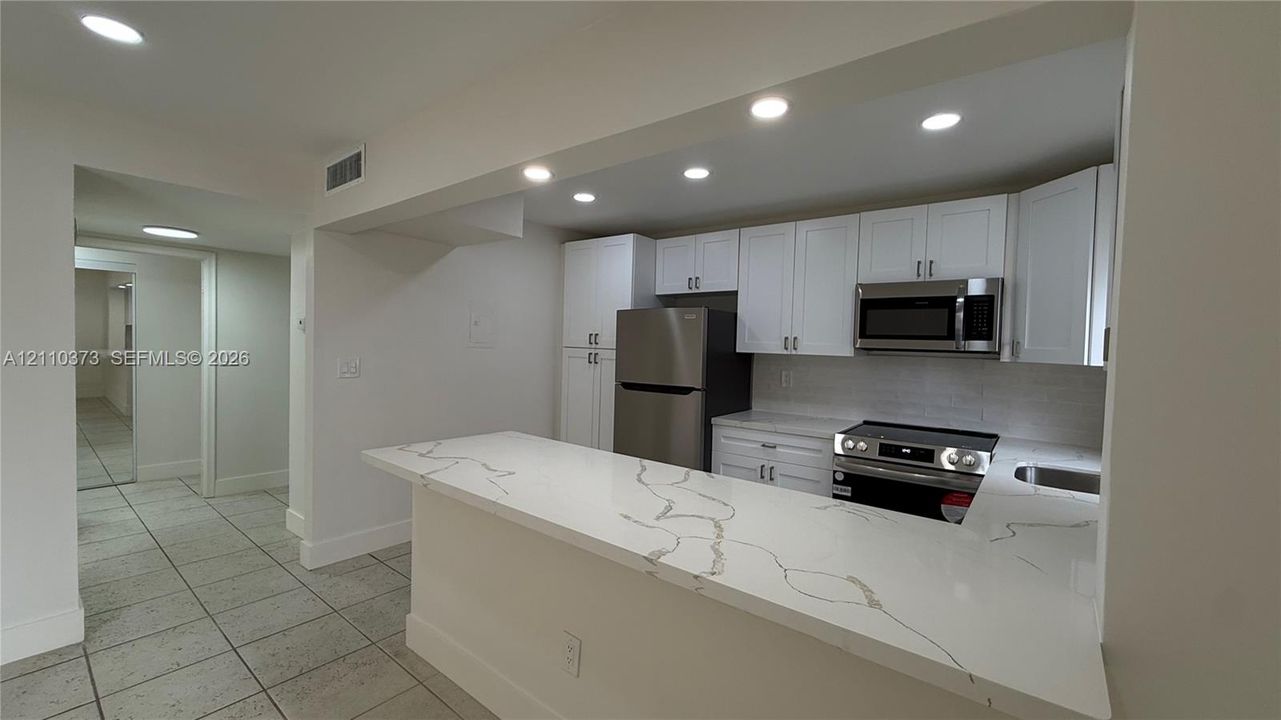 Kitchen featuring a quartz countertop peninsula, white shaker-style cabinetry, stainless steel appliances, and recessed lighting