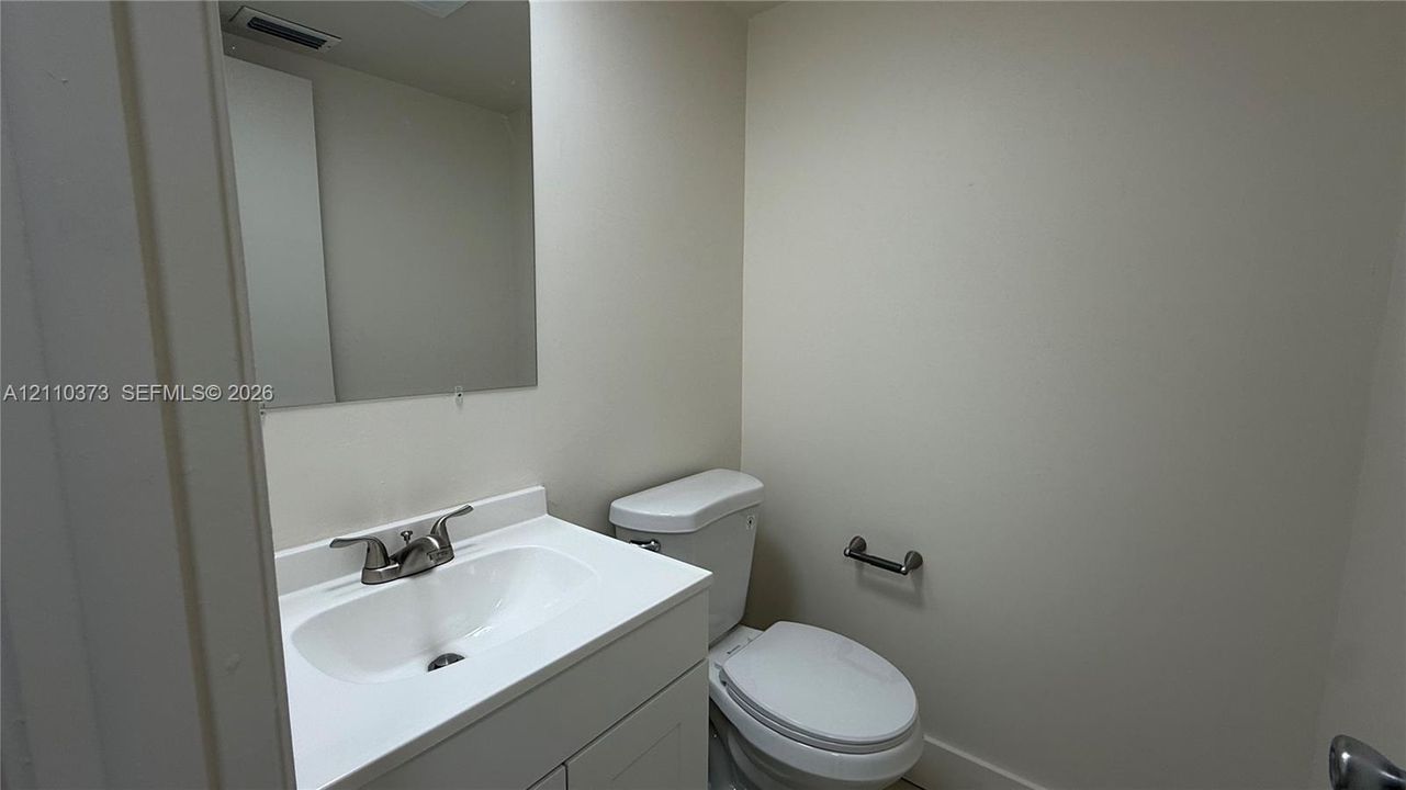 Vanity with a white integrated countertop and sink, metal dual-handle faucet, wall-mounted mirror, and standard porcelain toilet