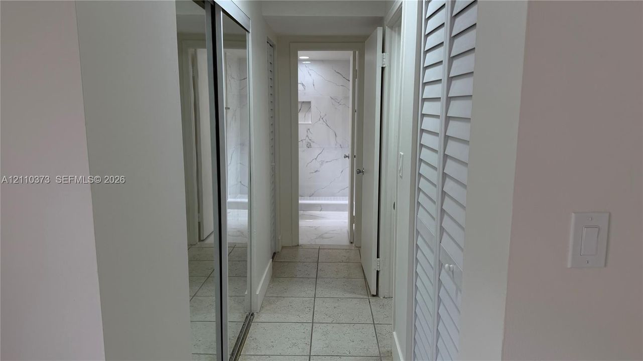 Hallway featuring mirrored sliding closet doors, white louvered closet doors, and ceramic tile flooring