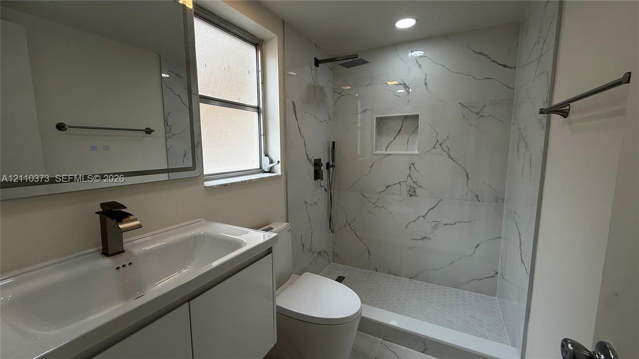 Bathroom featuring a vanity with an integrated basin, a wall-mounted mirror, a walk-in shower with large-format tile surround, a built-in shower niche, and a contemporary single-handle faucet