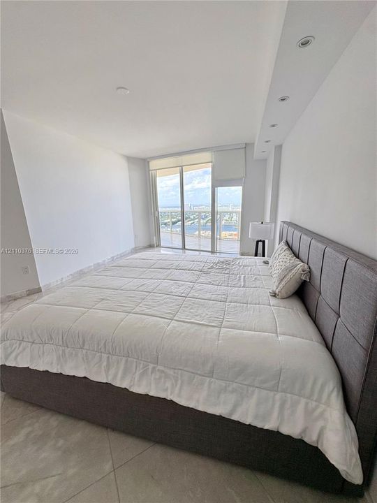 Floor-to-ceiling glass sliding doors opening to a balcony, polished stone-finish flooring, and recessed ceiling lighting