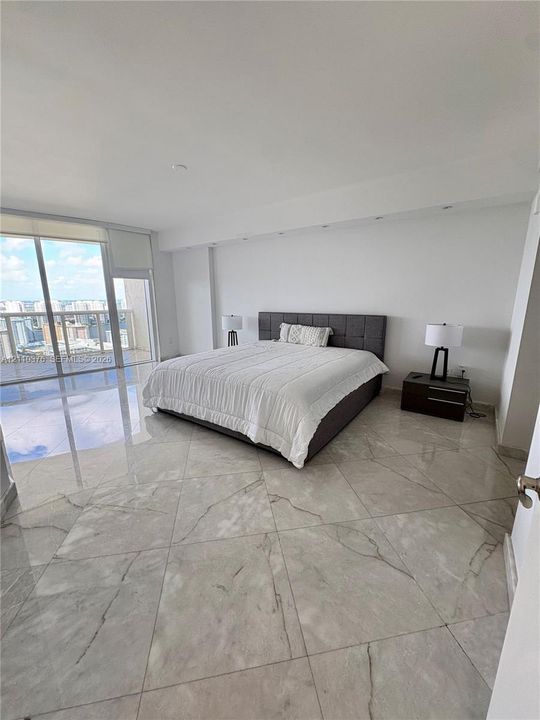 Floor-to-ceiling glass sliding doors, large-format polished tile flooring, recessed ceiling lighting, and a private balcony