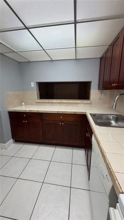 Kitchen featuring dark wood-finish cabinetry, tile countertops with a matching backsplash, a stainless steel sink with a pull-down faucet, and a tiled floor