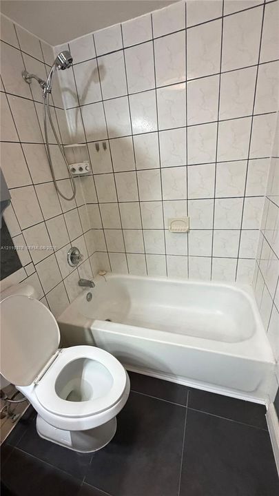 Bathtub with integrated shower, wall-mounted handheld showerhead, ceramic tile surround, and large-format tile flooring