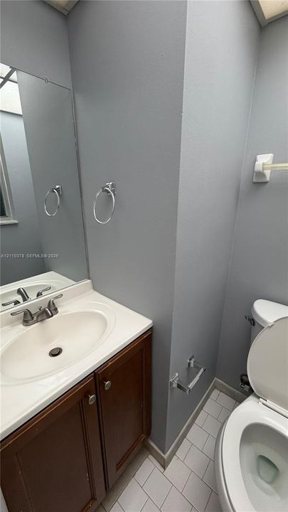 Vanity featuring a stone-composite countertop, undermount oval sink, wooden cabinetry, large wall-mounted mirror, and tile flooring
