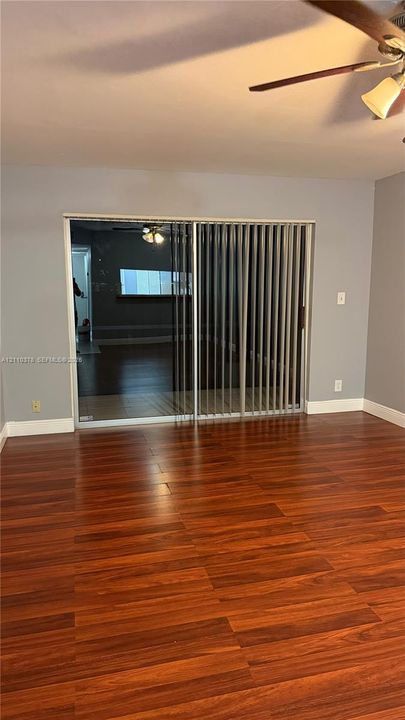 Interior space featuring wood-finish flooring, sliding glass doors with vertical blinds, and a ceiling-mounted light fixture with a fan