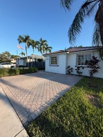Exterior featuring a white stucco facade, metal roof, paver driveway, grid-pattern windows, and established palm trees