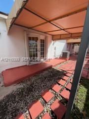 Covered patio with a structural overhead awning, multi-lite glass French doors, painted concrete flooring, and a stone-paver walkway
