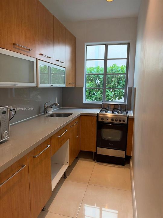 Kitchen featuring wood-finish cabinetry, stone-surface countertops, glass-front upper cabinets, stainless steel gas range, and large-format tile flooring