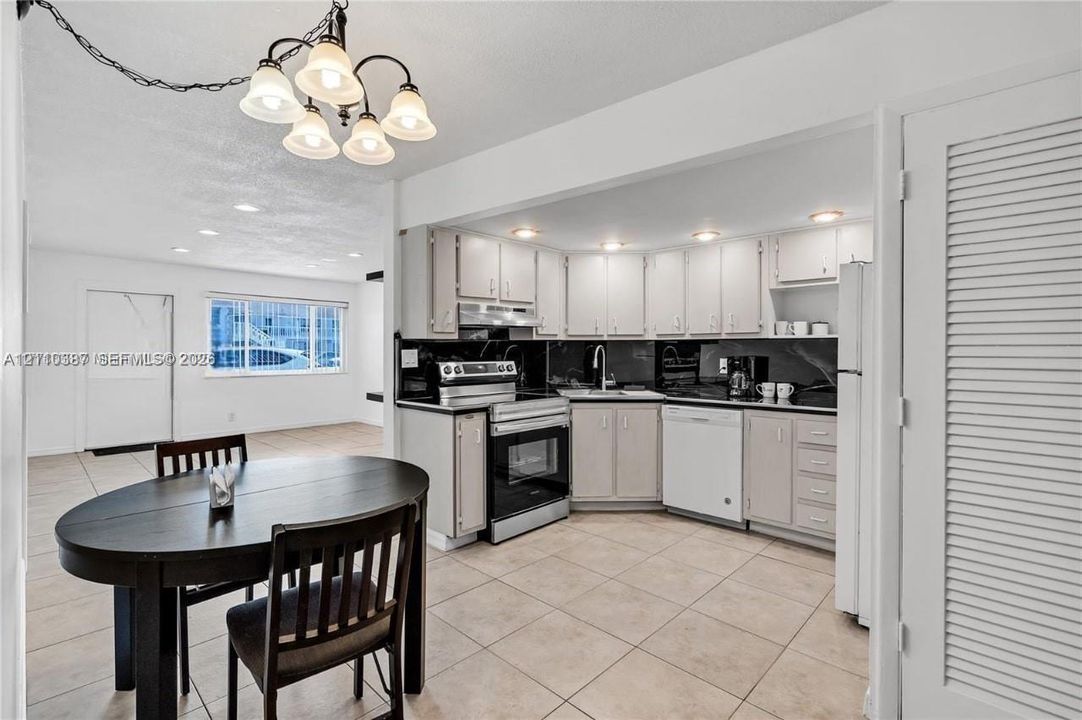 Kitchen featuring white shaker-style cabinetry, black stone countertops, stainless steel appliances, and ceramic tile flooring, complemented by a multi-light chandelier