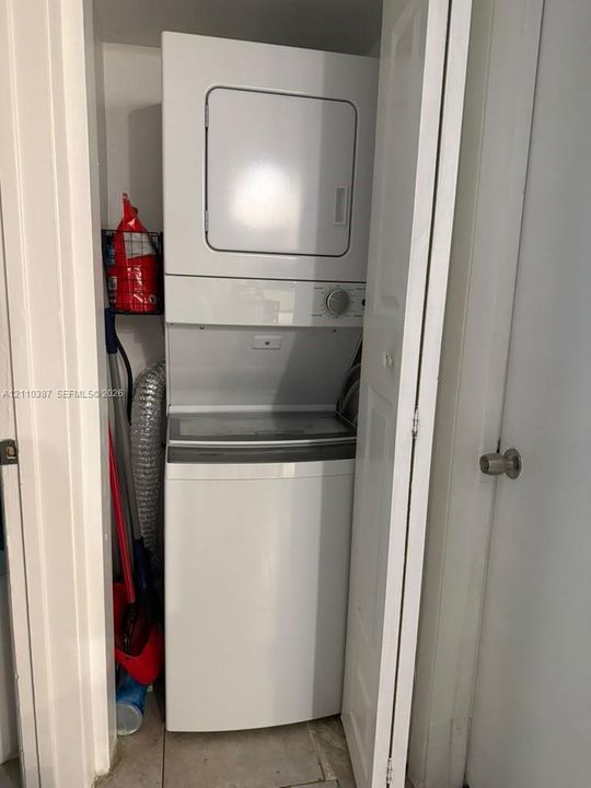 Stacked laundry unit featuring a white top-loading washer and integrated electric dryer
