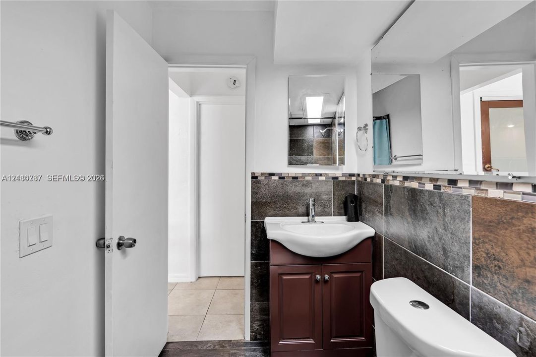 Bathroom featuring a dark wood-finish vanity with a ceramic basin, chrome faucet, expansive wall-to-wall mirror, and floor-to-ceiling tilework with mosaic decorative accents