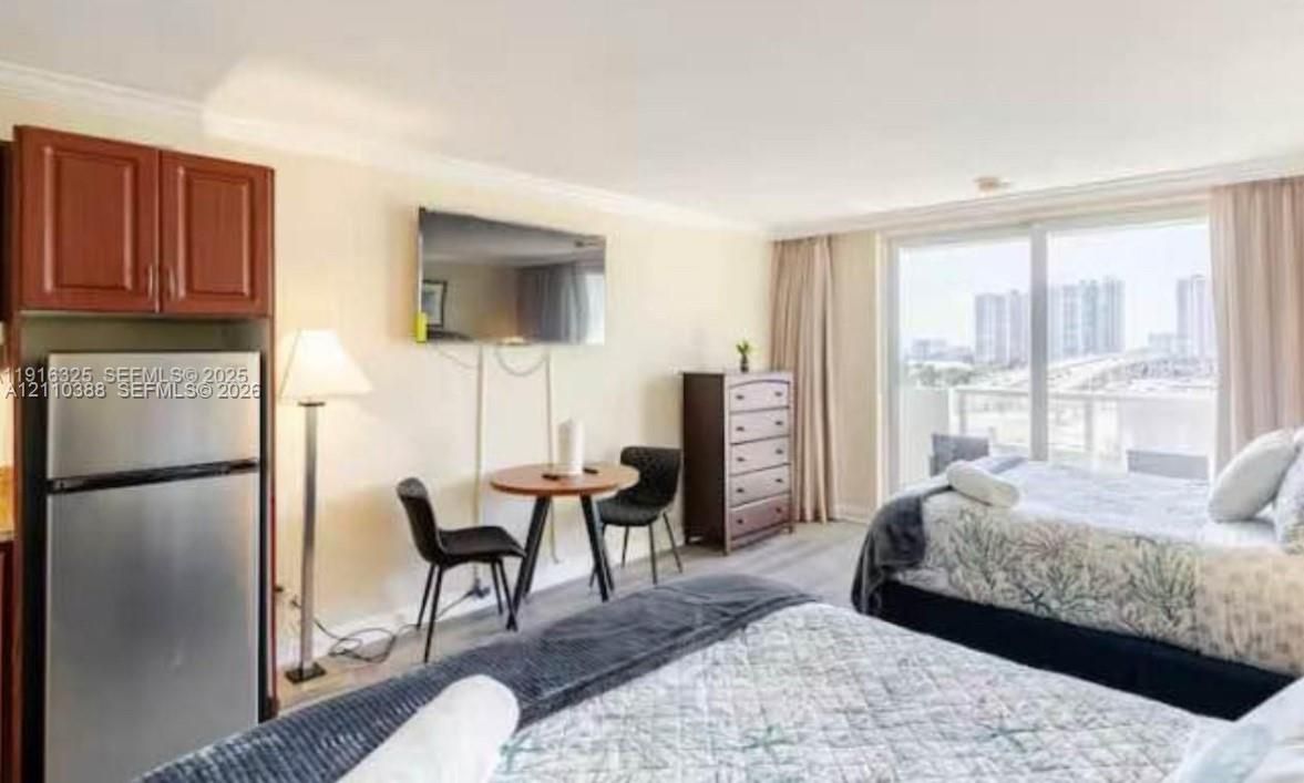Studio featuring wood-finish flooring, a stainless steel refrigerator, dark wood-finish cabinetry, and glass sliding doors providing exterior exposure
