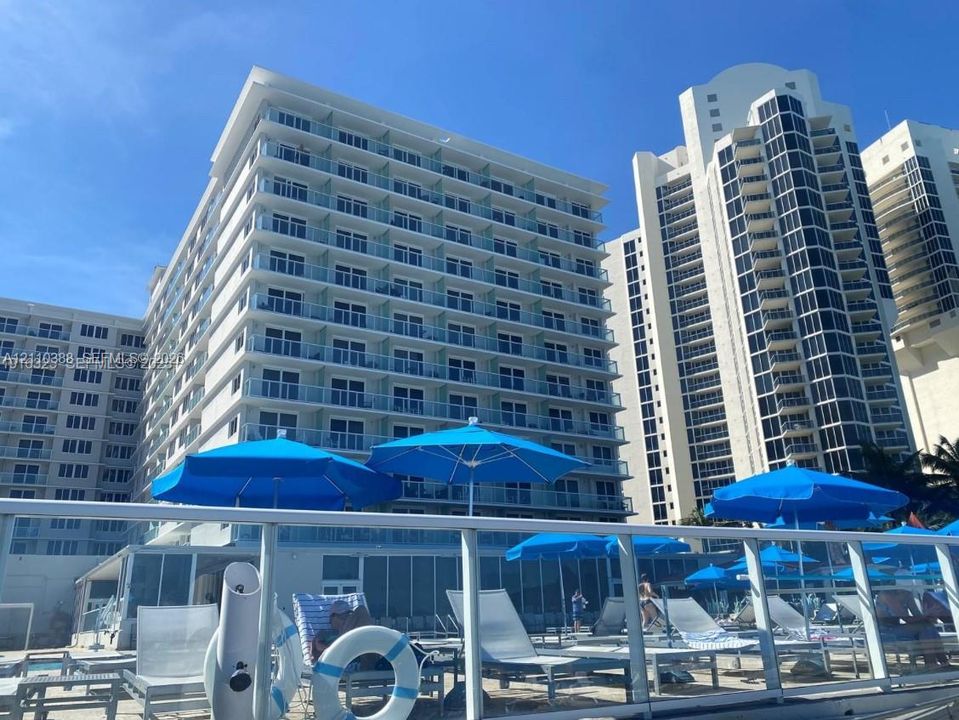 High-rise residential exterior featuring expansive glass-railed balconies, a multi-story concrete facade, and a ground-level swimming pool deck