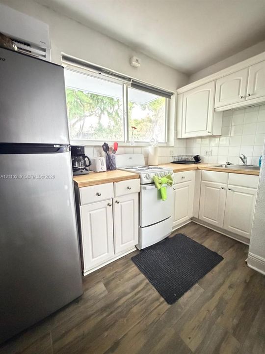 Kitchen featuring white shaker-style cabinetry, wood-finish countertops, stainless steel refrigerator, tile backsplash, and wood-finish flooring