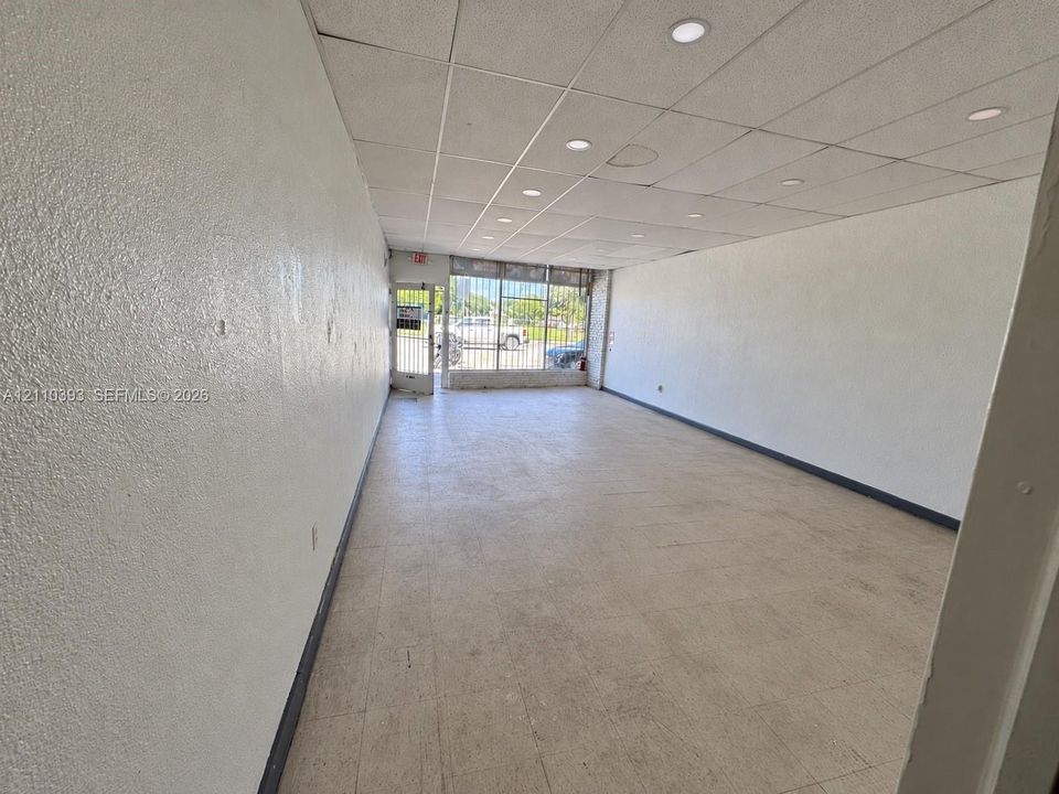 Open floor plan featuring tile flooring, drop ceiling with recessed lighting, and expansive glass-front entry with security grating
