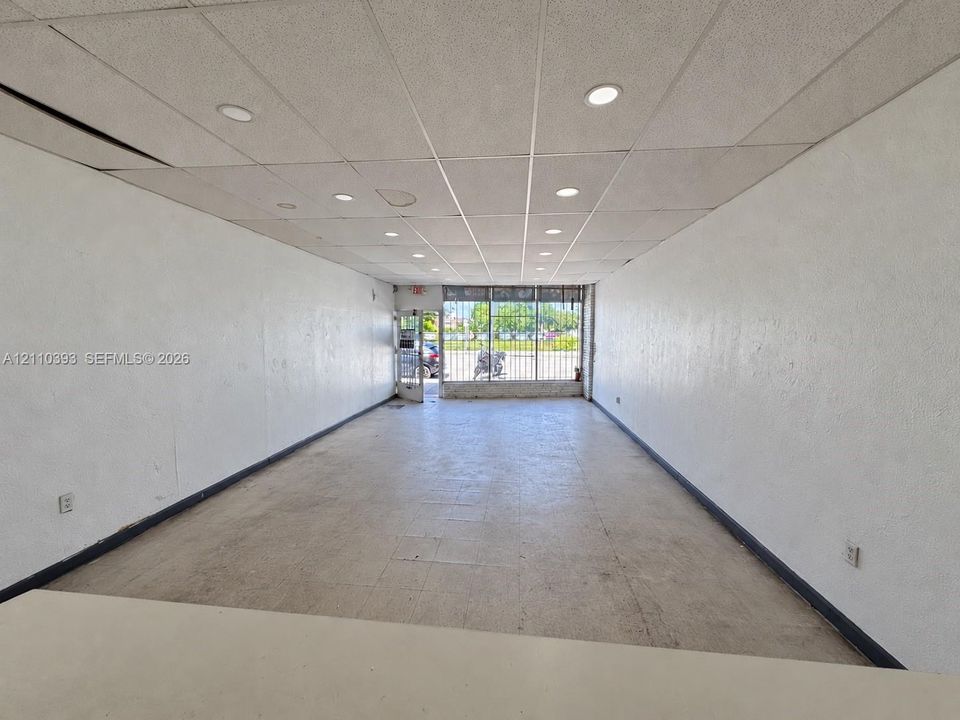 Open-concept interior featuring a drop ceiling with recessed lighting, tile flooring, and a large front window with metal security bars