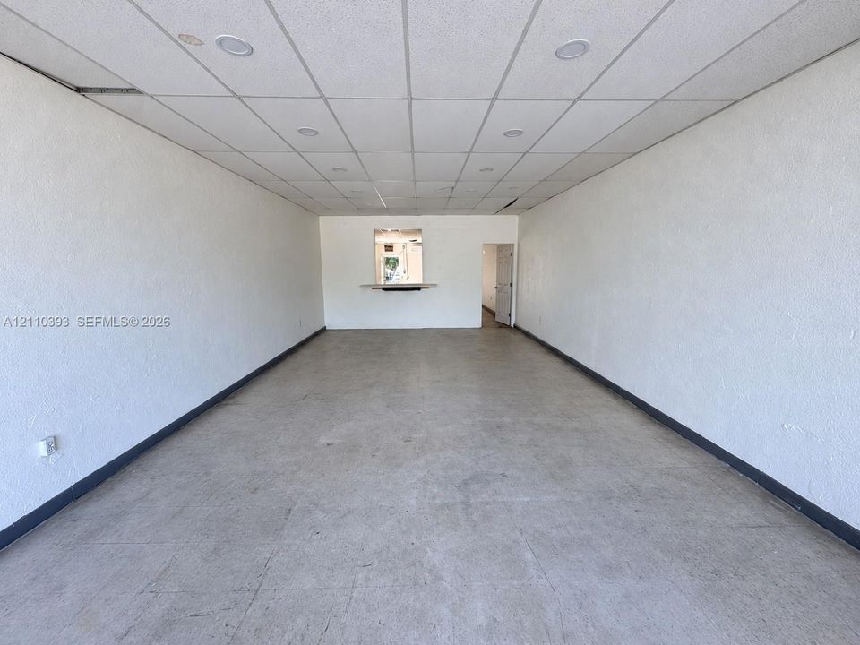 Open-concept interior featuring textured walls, dropped ceiling tiles, recessed lighting, and a service pass-through window with a built-in counter
