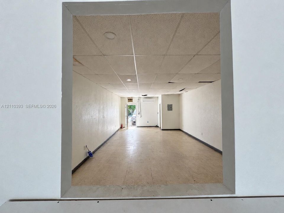 Open-plan interior space featuring a drop ceiling with recessed lighting, wall-mounted heating and cooling unit, and an exterior door