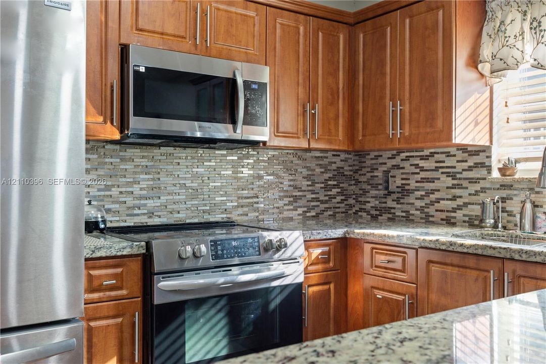 Kitchen featuring wood cabinetry, stainless steel appliances, stone-finish countertops, and a multi-toned linear mosaic tile backsplash