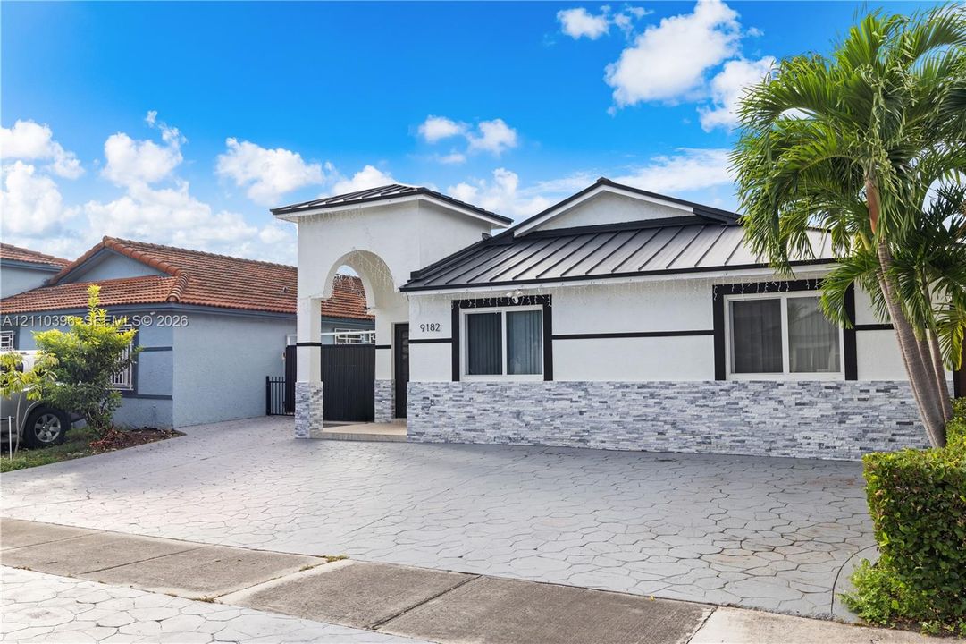 Exterior featuring a metal roof, arched covered entryway, stone-veneer facade, and patterned concrete driveway