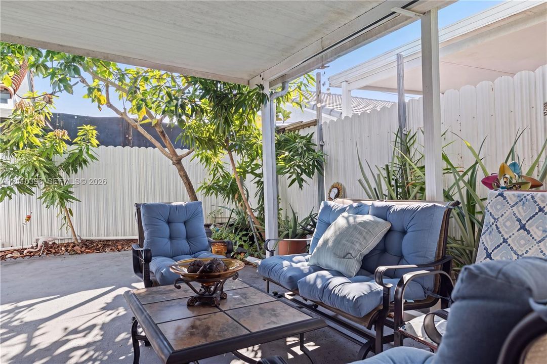 Covered concrete patio featuring a white privacy fence and mature landscaping